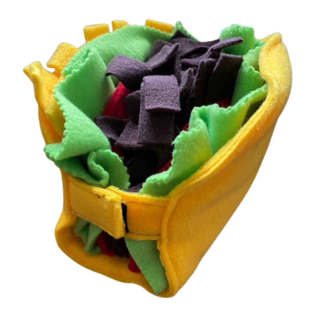 A colour image of a handmade dog toy in the style of a taco. It is made from yellow, green, red and brown fleece fabric and opens to lay flat or close.
